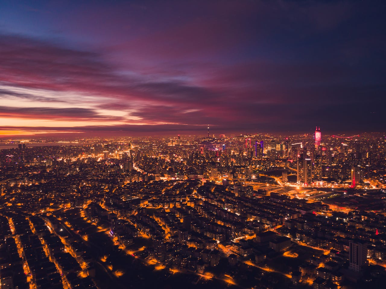 Aerial view of modern city with glowing buildings located in downtown at night time with dark cloudy sky